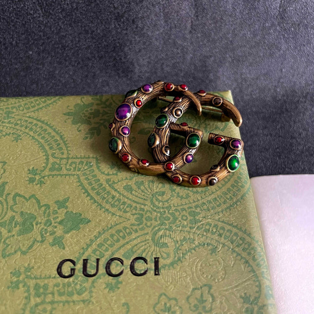 GUCCI 26S INTERLOCKING G MULTICOLOR GEM LOGO BROOCH IN ANTIQUE GOLD TONE METAL 625634